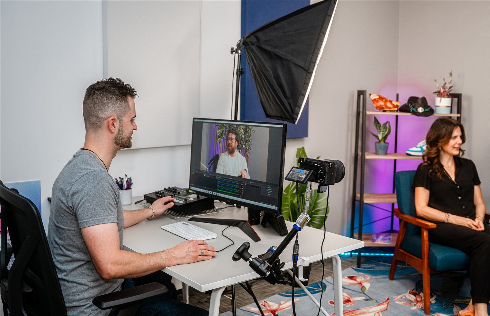 A studio manager at the editing monitor, with a guest seated in the background