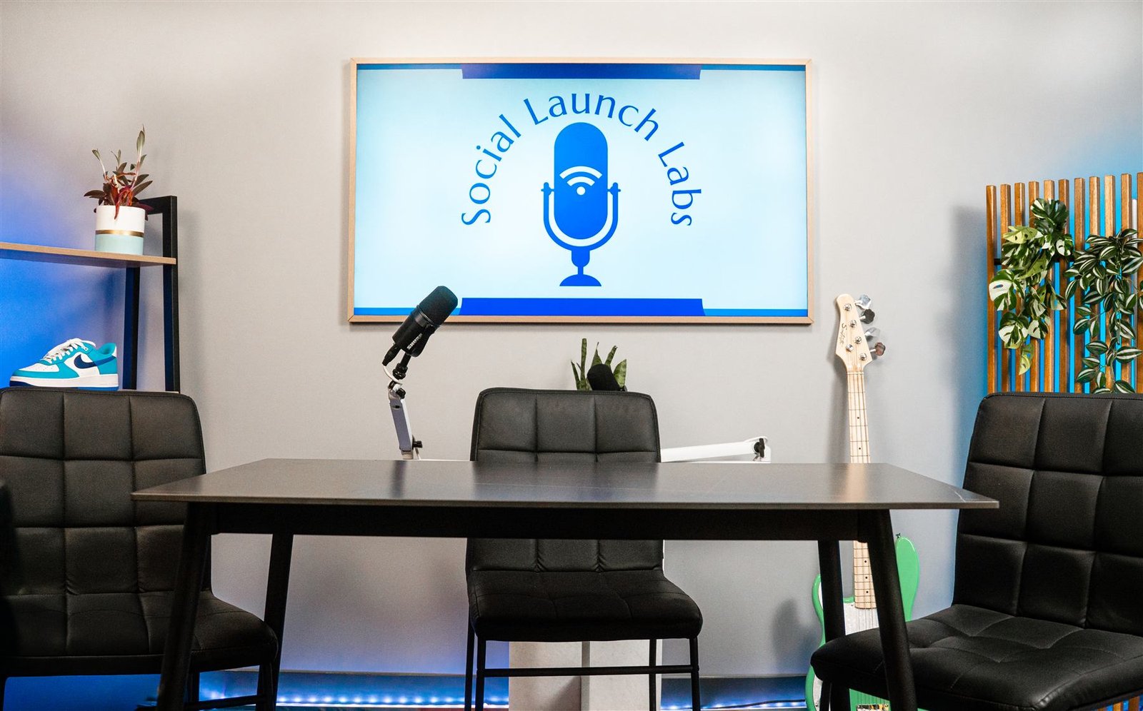 Podcast table setup with black chairs, a boom microphone, and the Social Launch Labs logo displayed on a wall-mounted screen